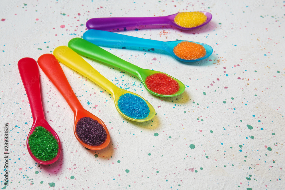 Spoons with color sugar on light background