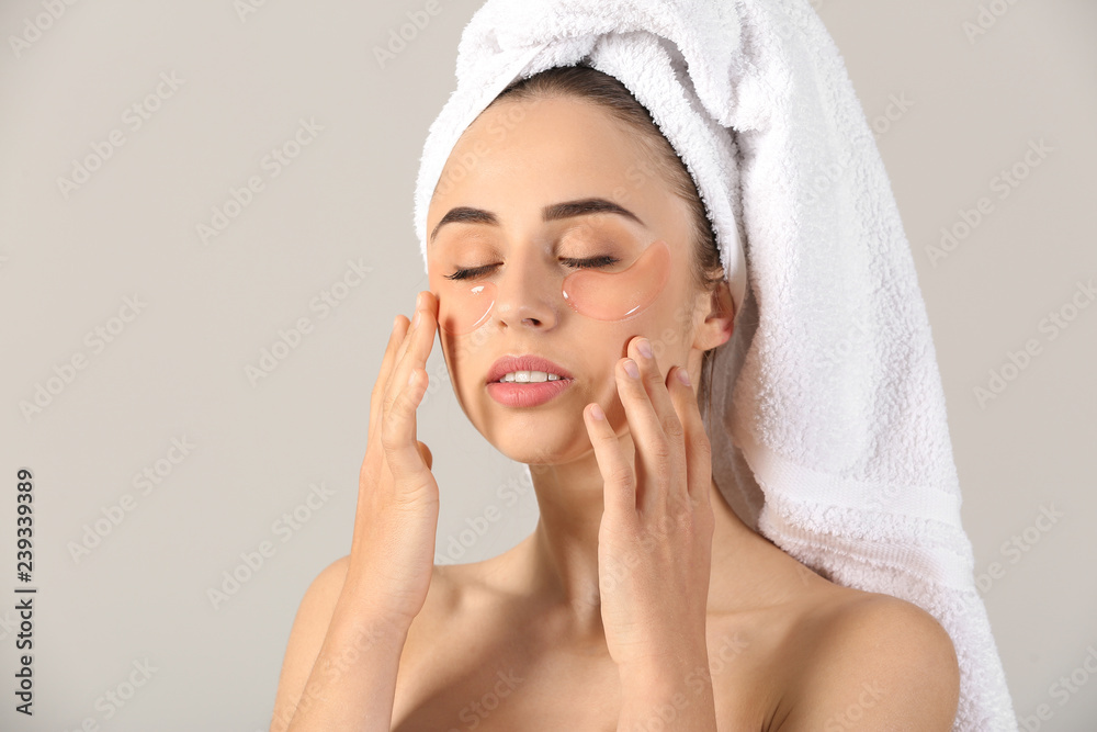 Beautiful young woman with under-eye patches on light background