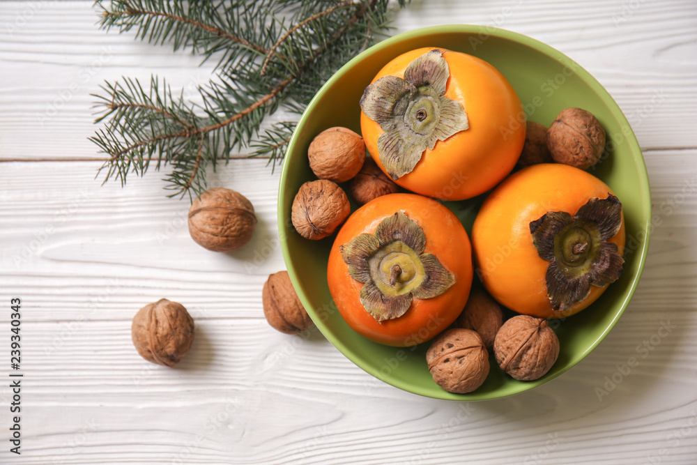 Bowl with tasty ripe persimmons and walnuts on white wooden table