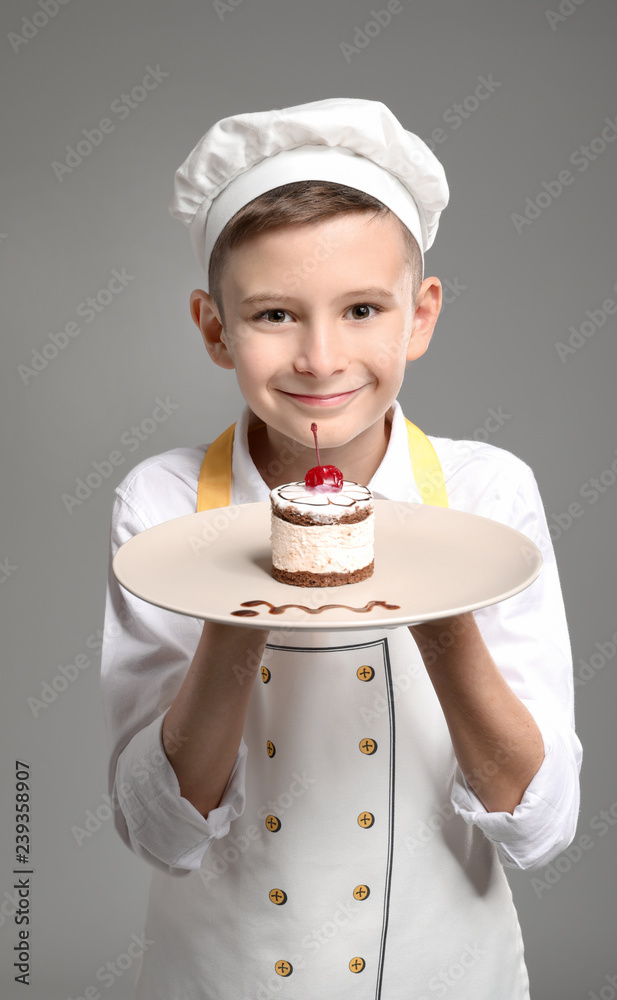 Cute little chef with tasty dessert on grey background