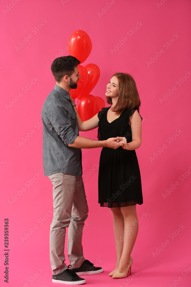 Loving young couple with heart-shaped balloons on color background. Celebration of Saint Valentines