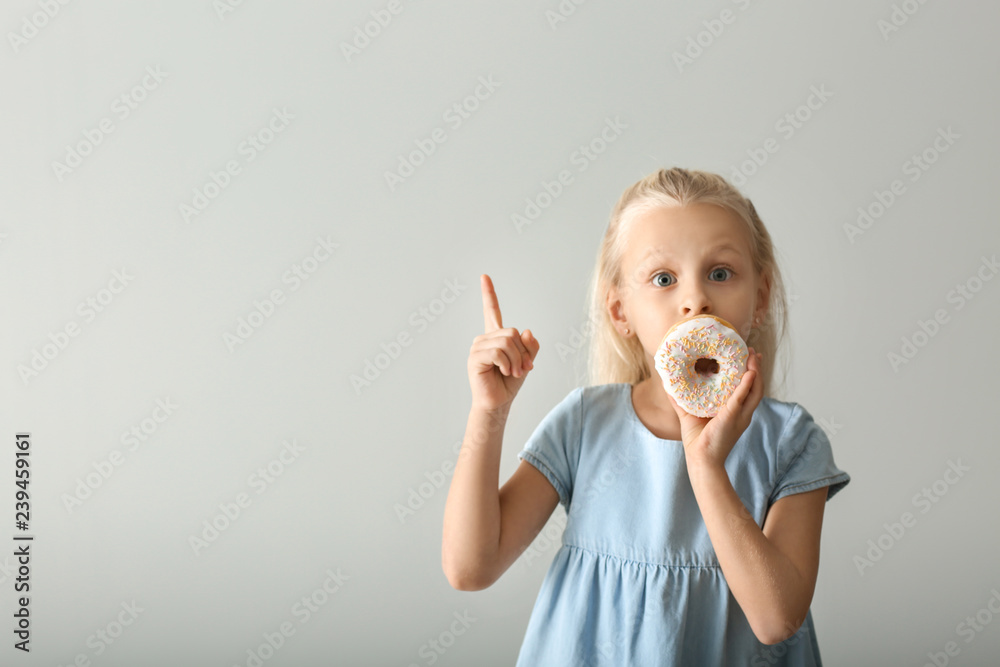 浅色背景下有甜甜圈和竖起食指的可爱小女孩