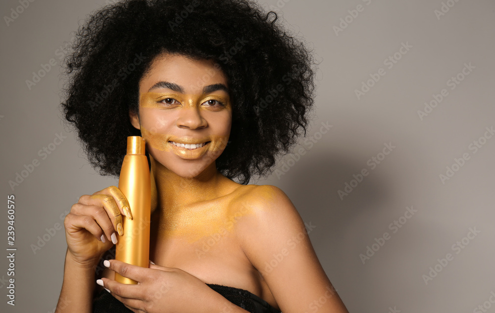 African-American woman with golden paint on her body and cosmetics against grey background