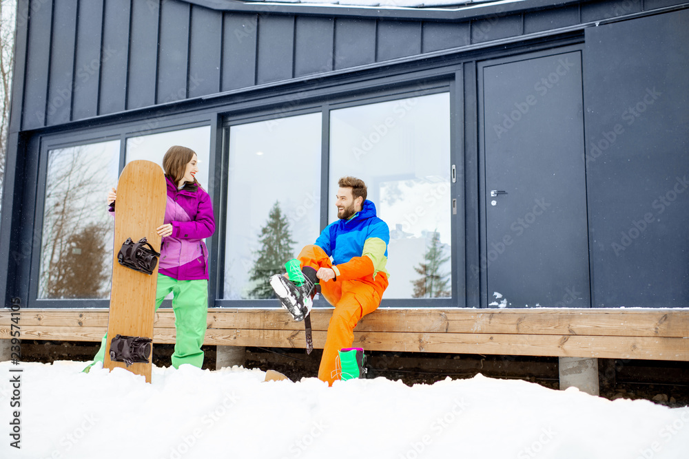 一对穿着滑雪服的年轻夫妇坐在t现代住宅的露台上准备单板滑雪