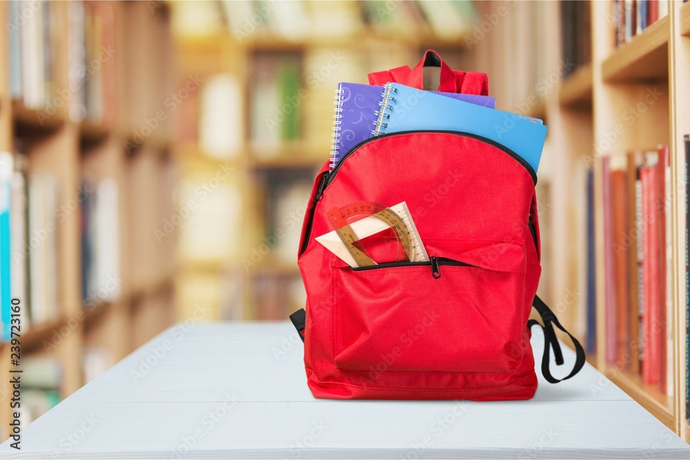 Open blue school backpack on withe table in library background.