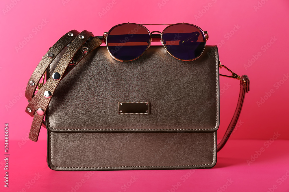 Female bag and sunglasses on color background