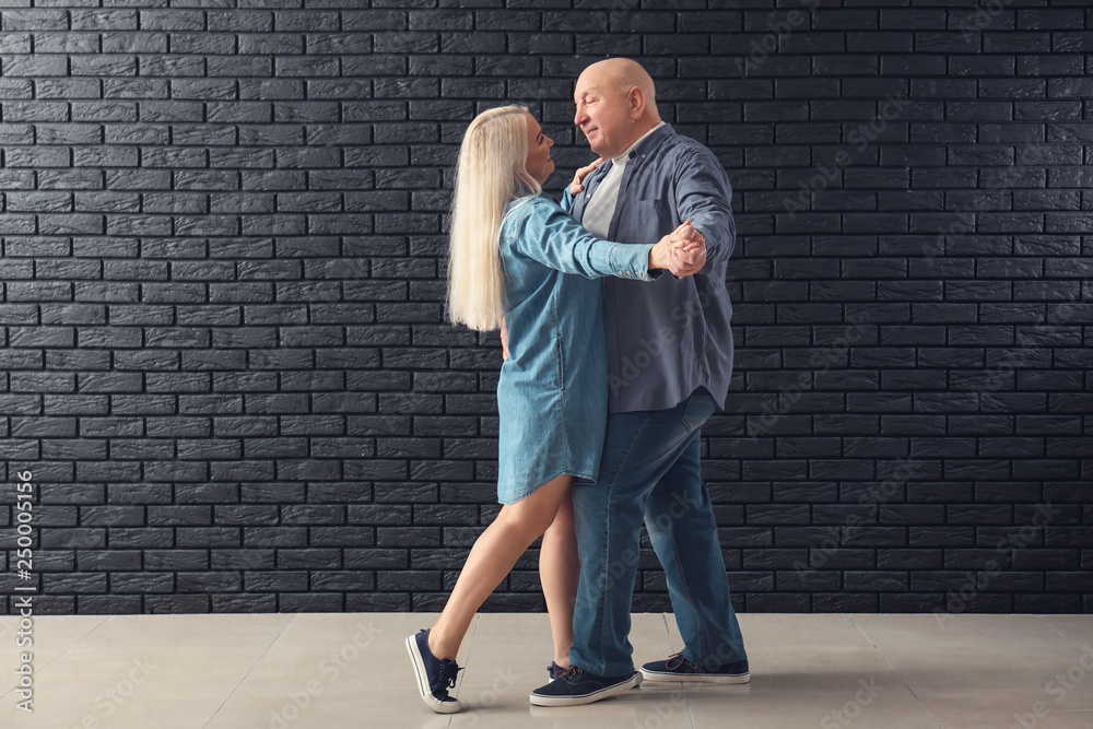 Cute elderly couple dancing against dark brick wall