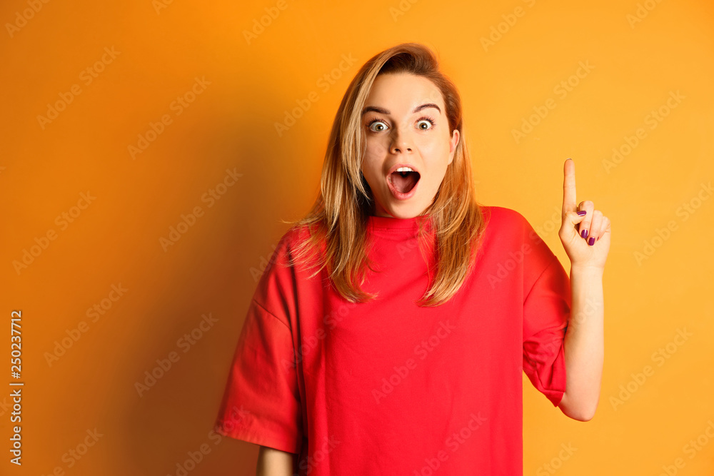 Portrait of emotional young woman with raised index finger on color background