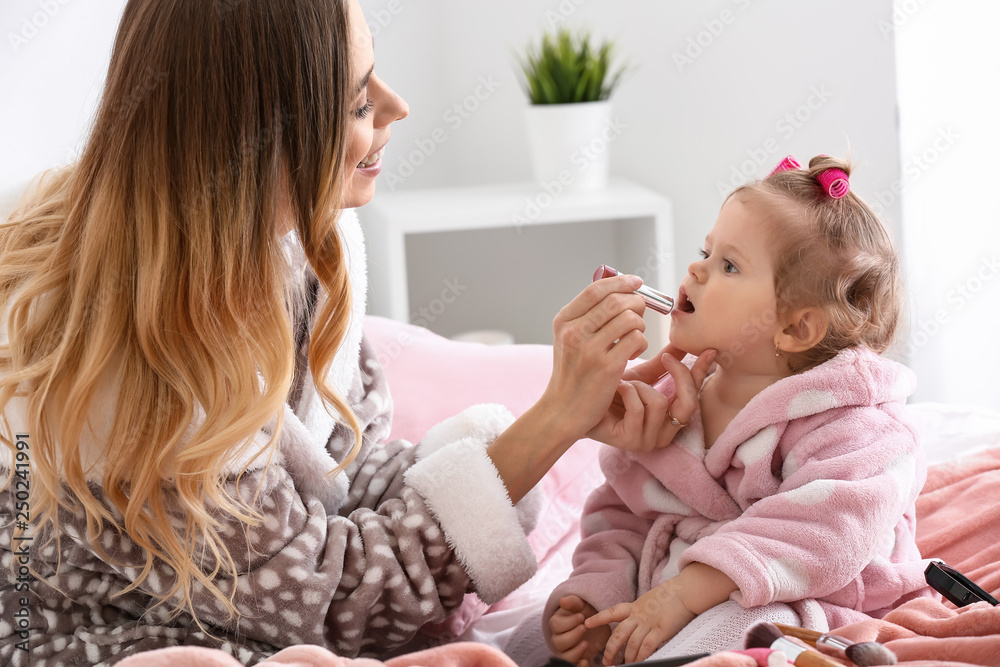 Young woman with her cute little daughter playing with cosmetics at home