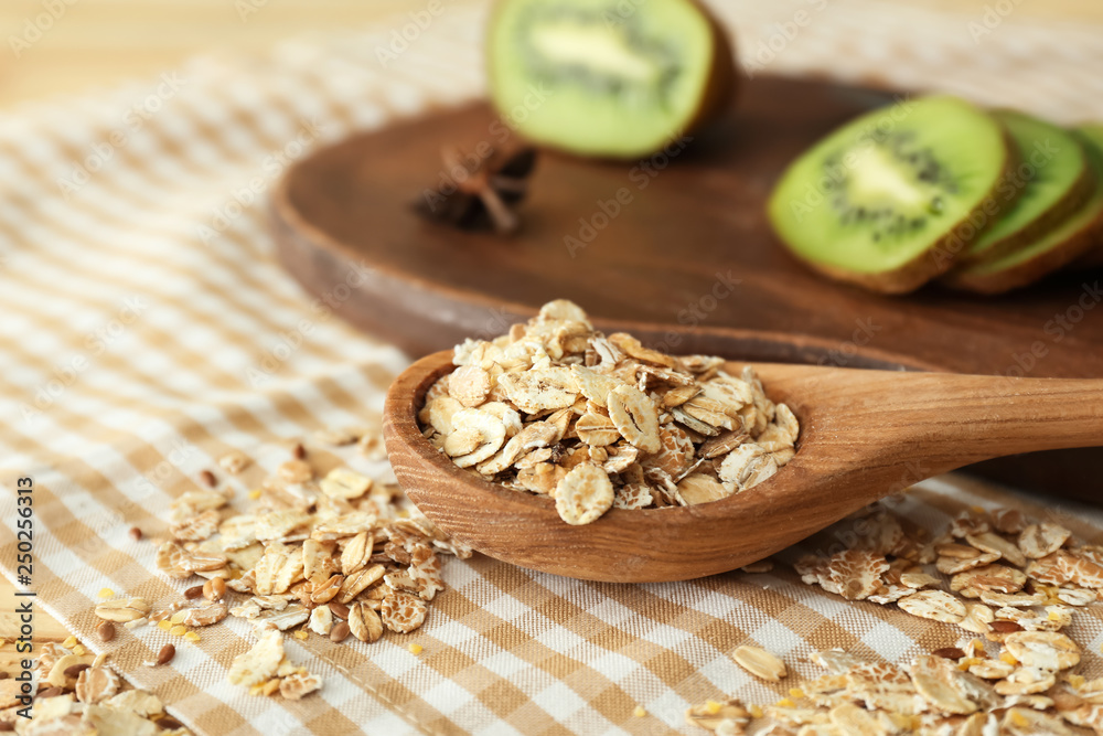 Spoon with raw oatmeal and kiwi on table