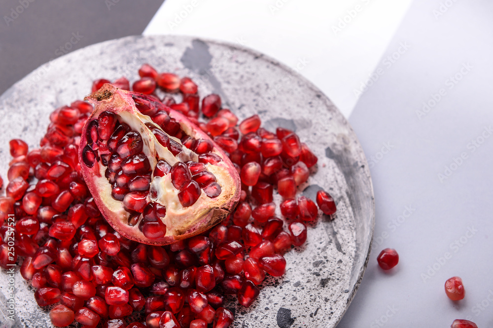 Plate with piece of ripe pomegranate and seeds on table