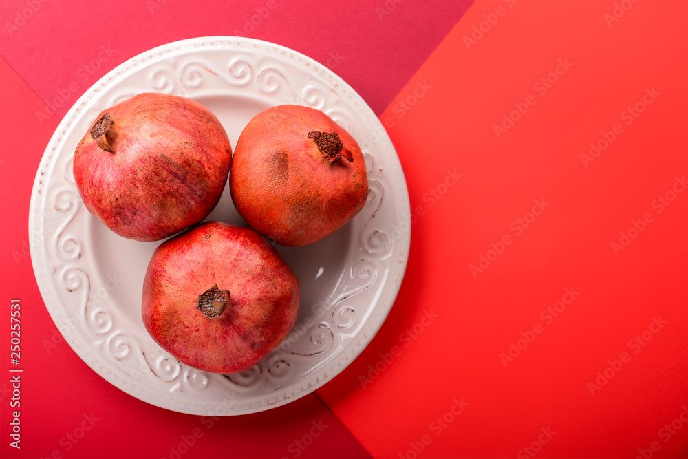 Plate with ripe pomegranates on color background