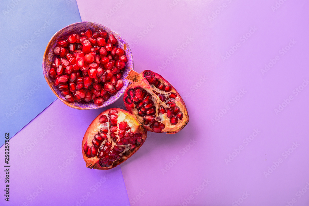 Pieces of ripe pomegranate and bowl with seeds on color background