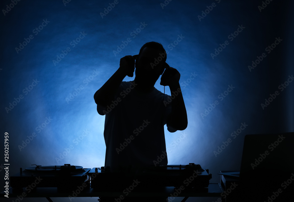 Silhouette of male DJ playing music on color background