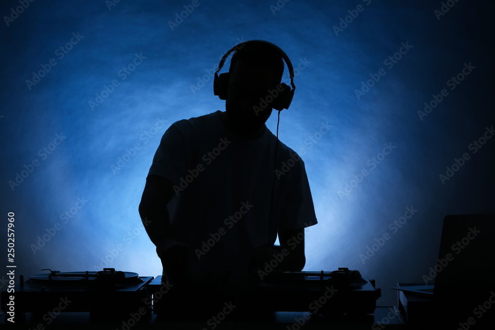 Silhouette of male DJ playing music on color background