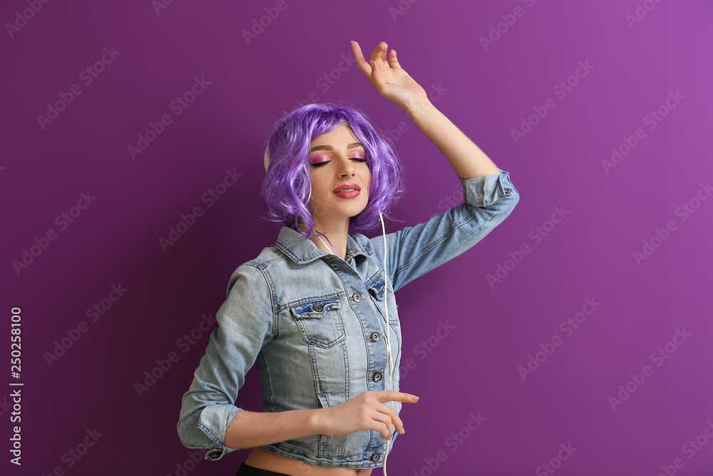 Beautiful young woman with headphones dancing against color background