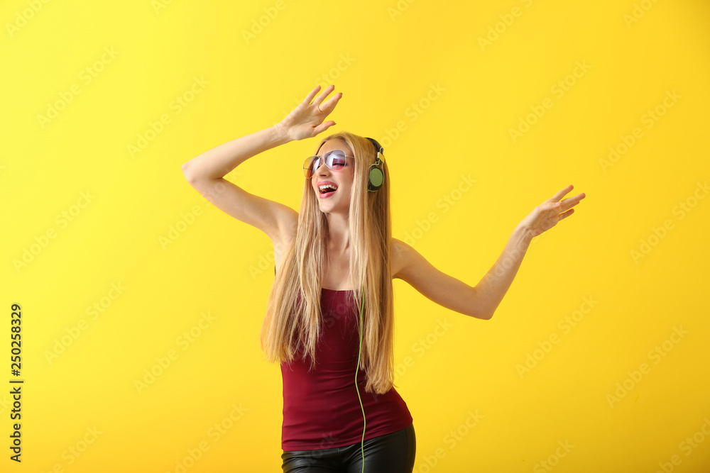 Beautiful young woman with headphones dancing against color background