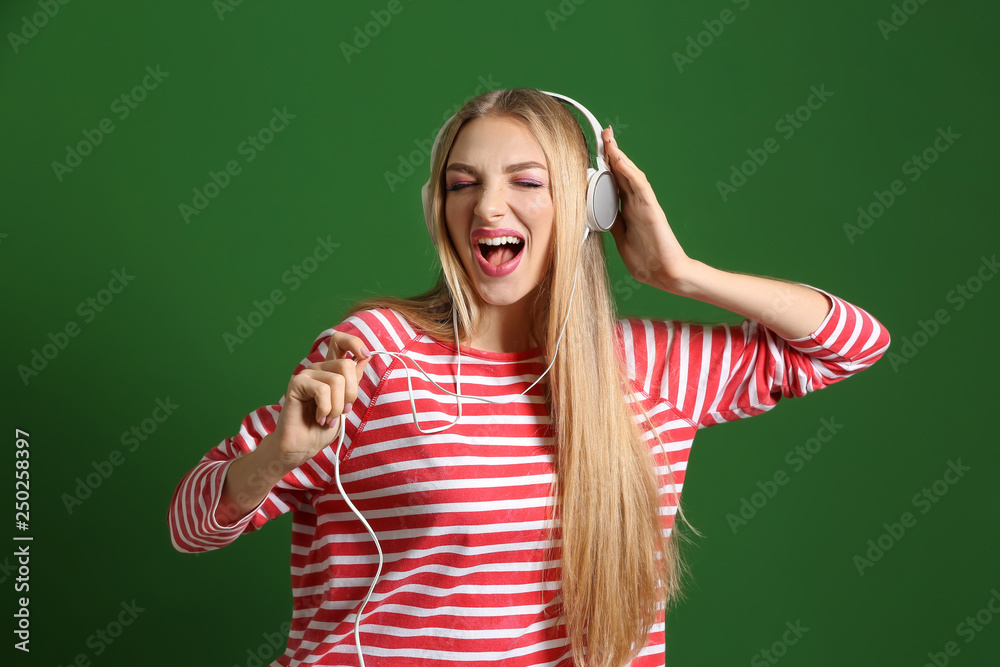 Beautiful young woman with headphones dancing against color background