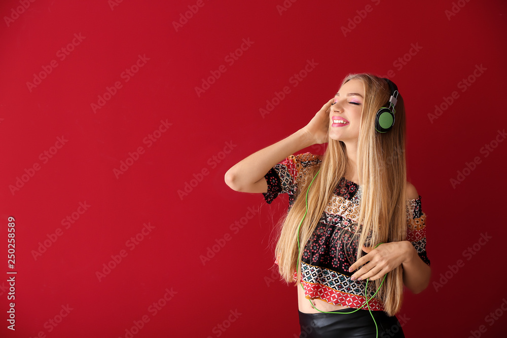 Beautiful young woman with headphones dancing against color background