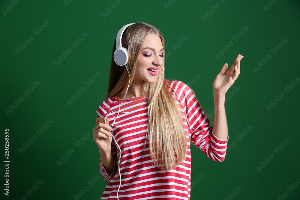 Beautiful young woman with headphones dancing against color background