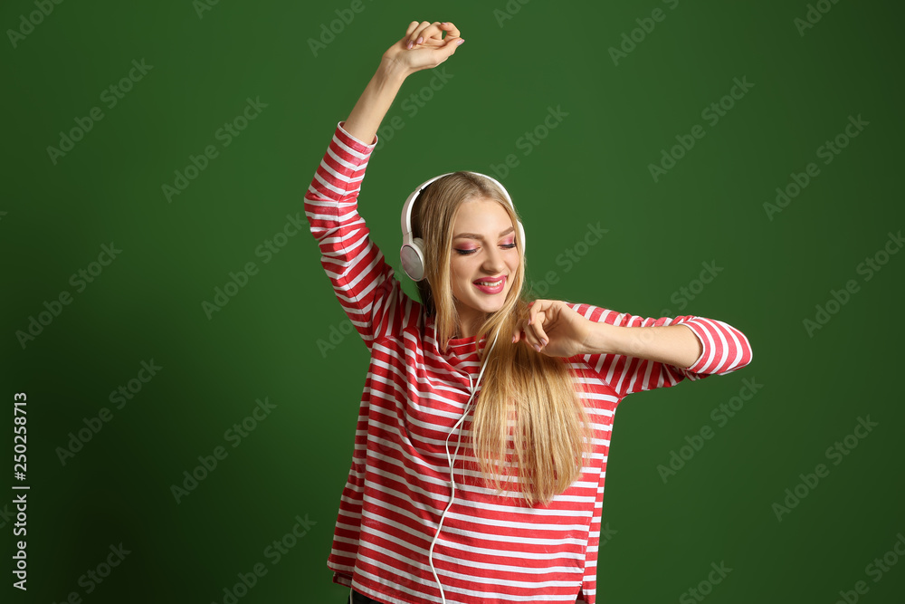 Beautiful young woman with headphones dancing against color background