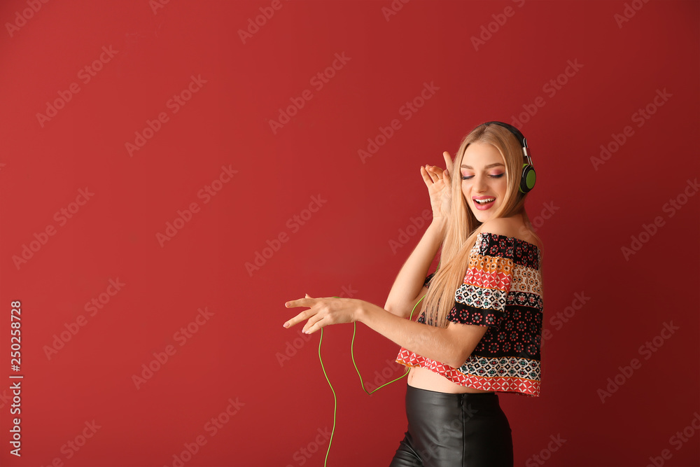 Beautiful young woman with headphones dancing against color background