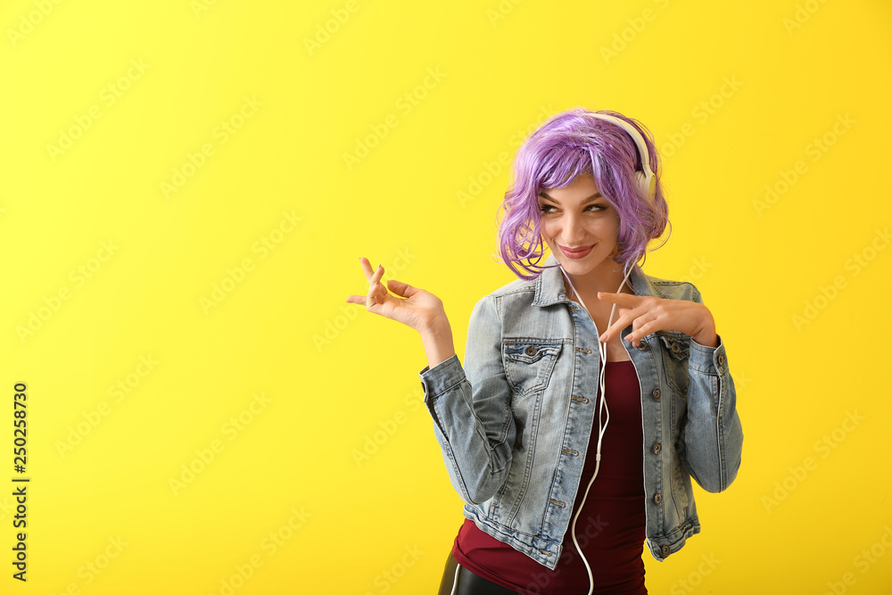 Beautiful young woman with headphones dancing against color background