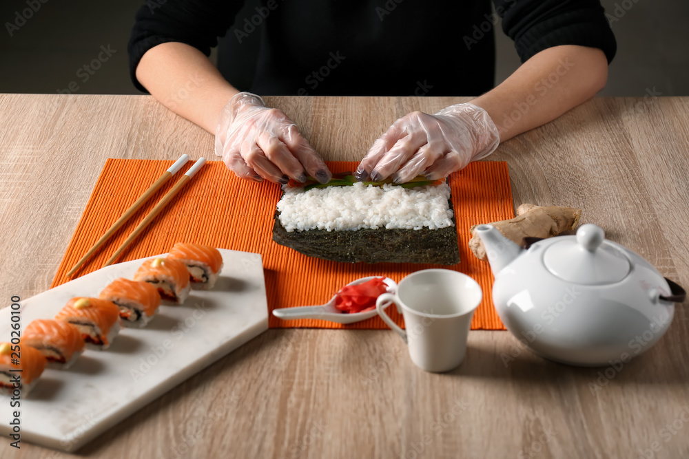 Woman making tasty sushi rolls at table