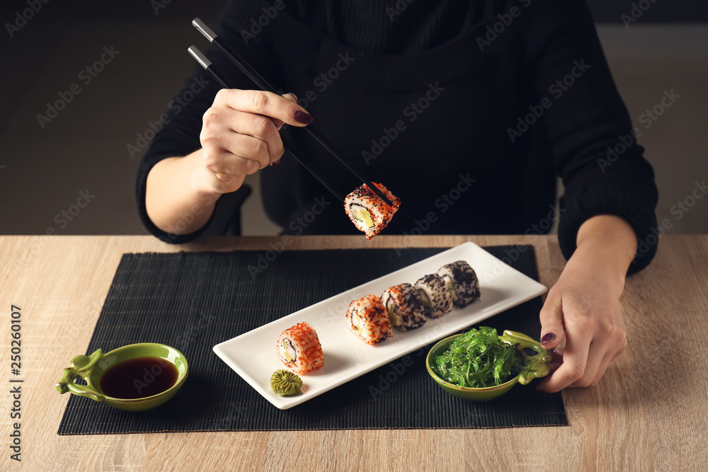 Woman eating tasty sushi rolls at table