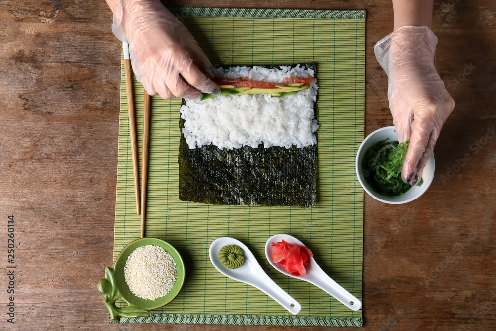 Woman making tasty sushi rolls at table