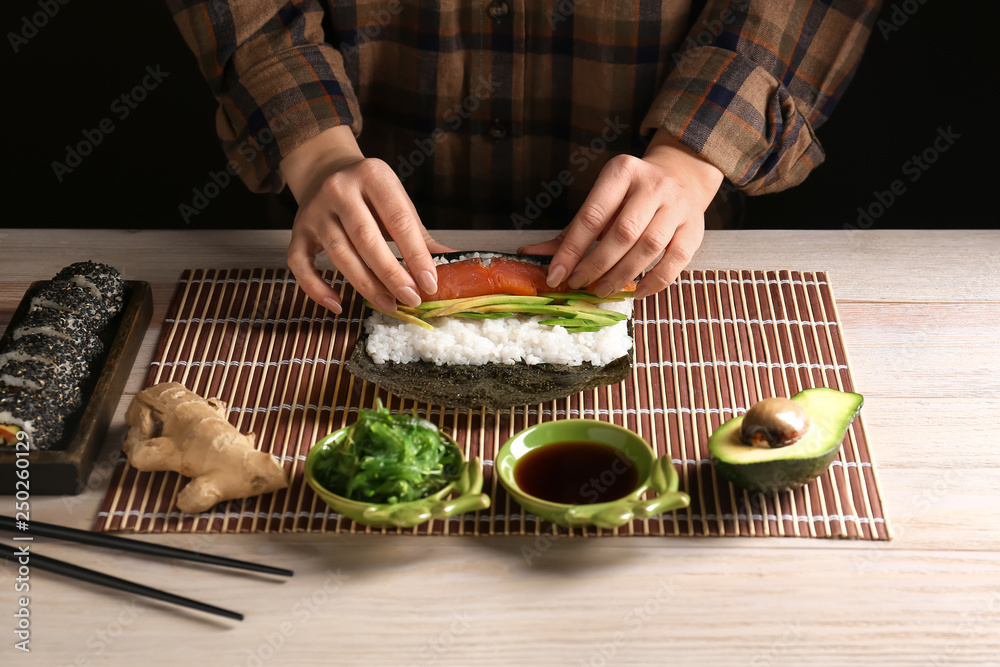 Woman making tasty sushi rolls at table