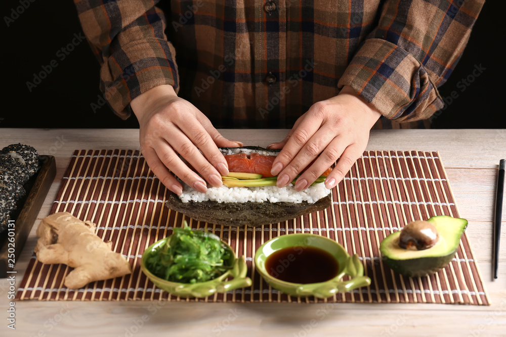 Woman making tasty sushi rolls at table