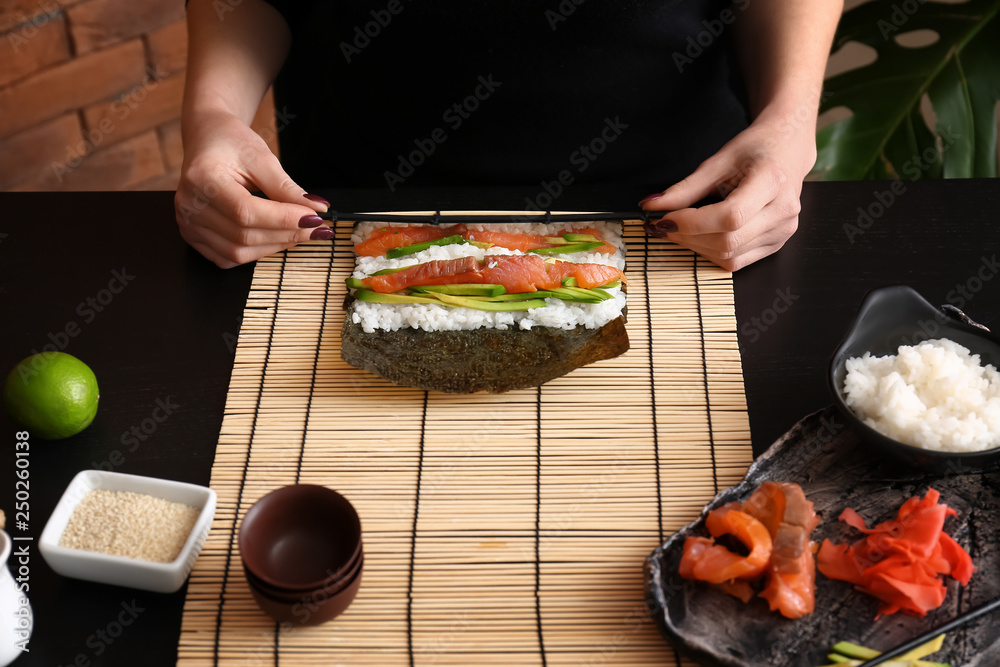 Woman making tasty sushi rolls at table