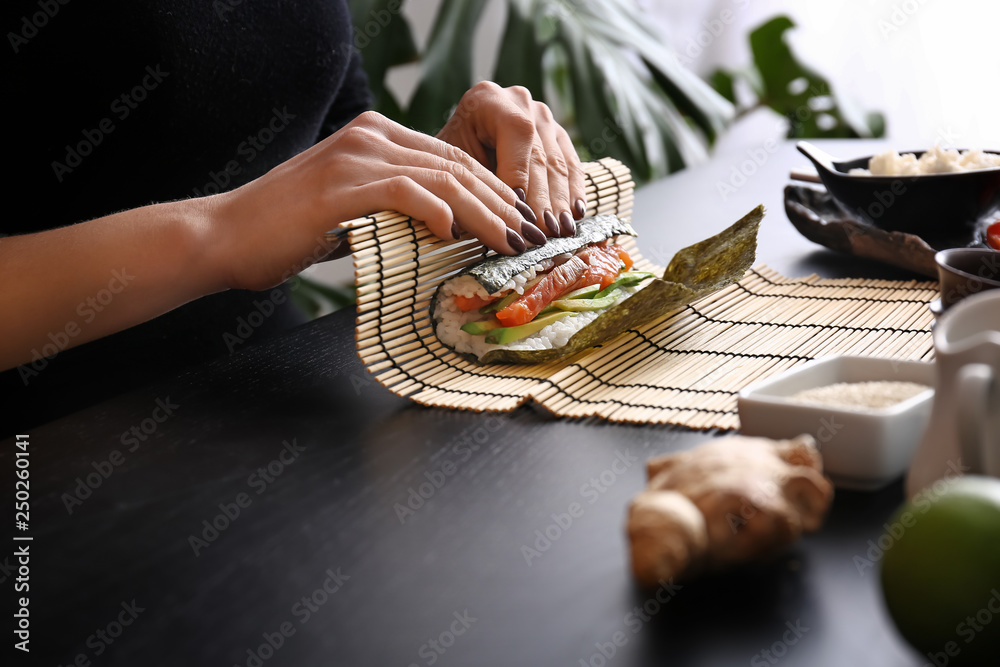 Woman making tasty sushi rolls at table