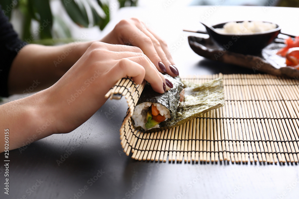 Woman making tasty sushi rolls at table