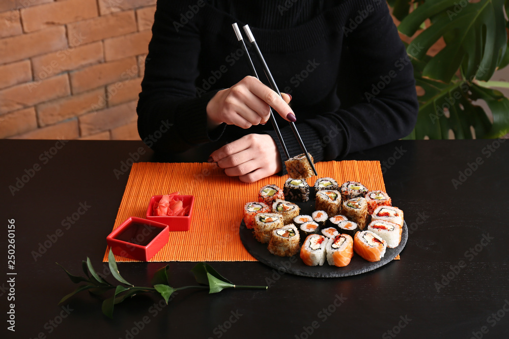 Woman eating tasty sushi rolls at table