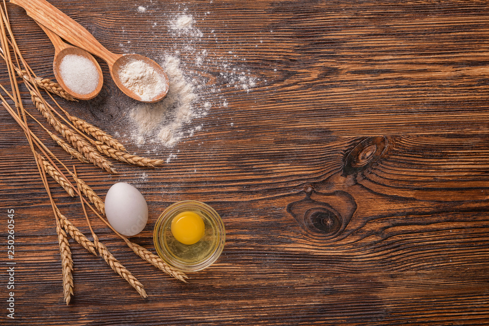 Eggs and spoons with flour on wooden table