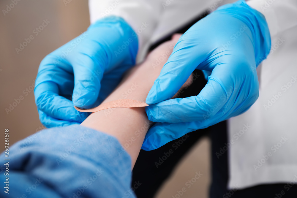 Doctor applying plaster onto hand of young woman, closeup