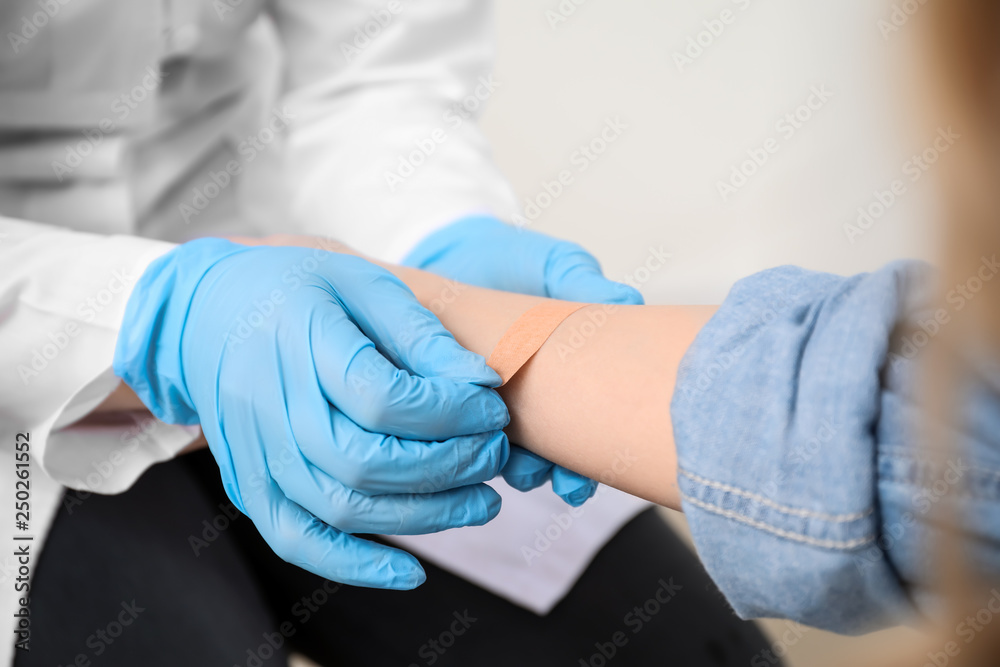 Doctor applying plaster onto hand of young woman, closeup