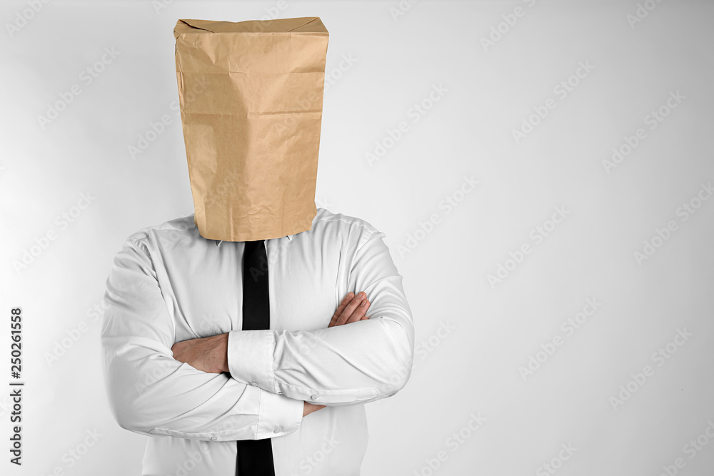 Businessman with paper bag on his head against light background