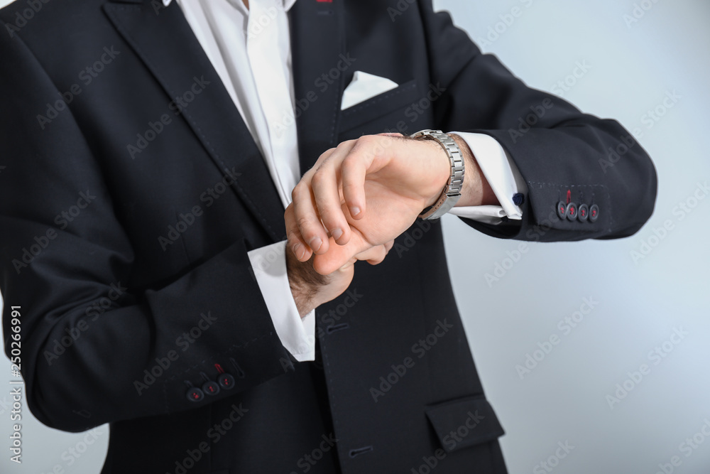 Handsome fashionable man in formal clothes looking at watch against light background, closeup