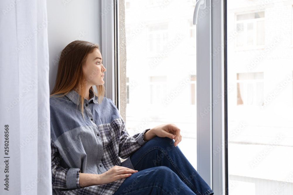 Young woman sitting on window sill at home