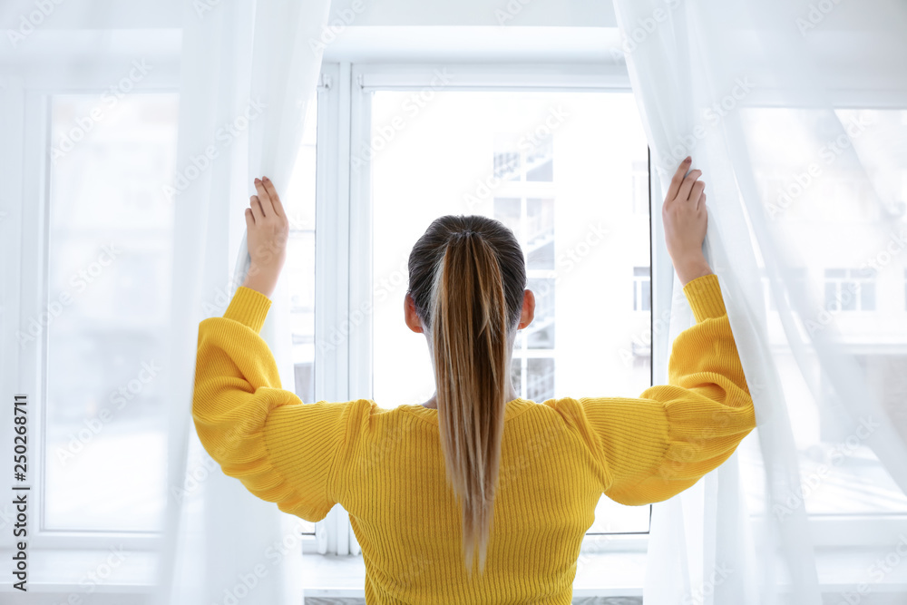 Young woman opening curtains in morning