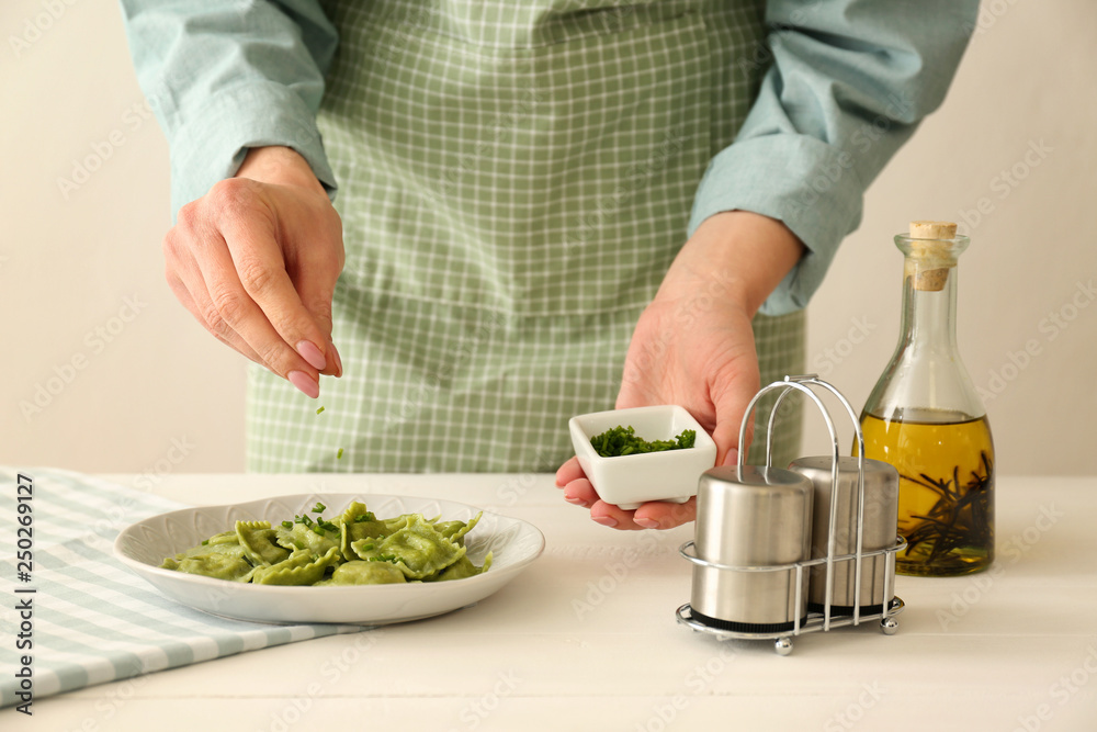 Chef sprinkling tasty ravioli on plate with herbs