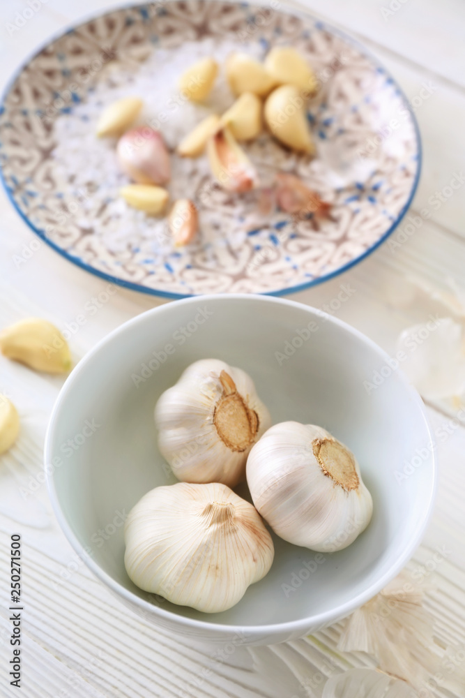 Bowl with fresh garlic on white wooden background