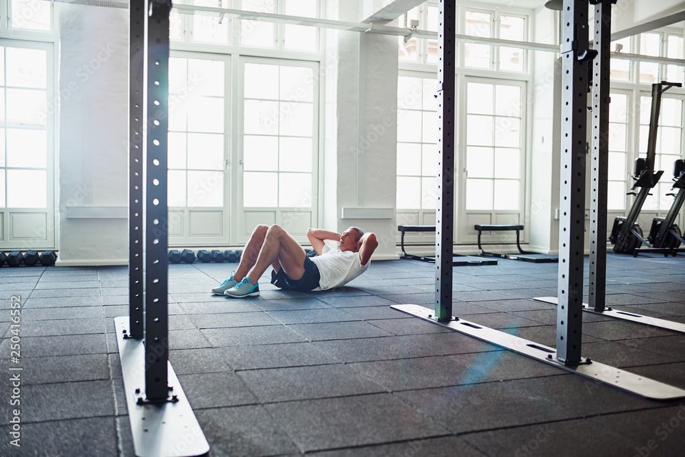 Mature man doing sit ups on a gym floor