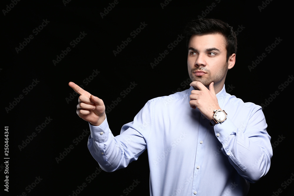 Handsome young businessman pointing with finger on dark background