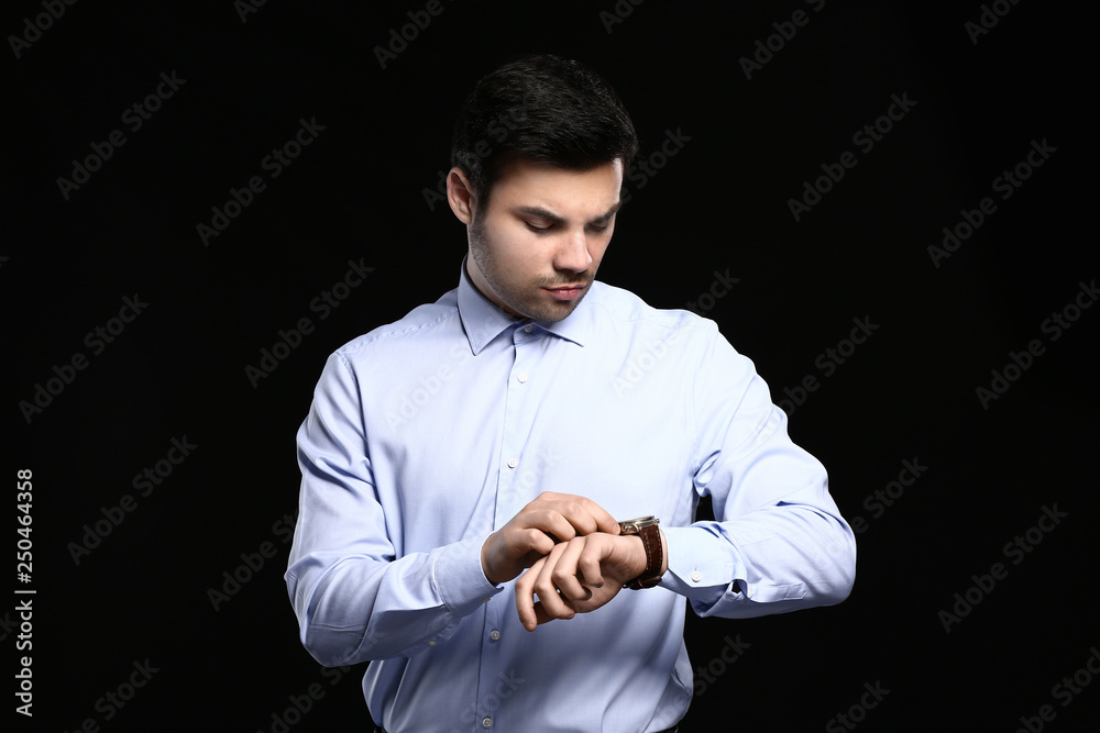 Handsome young businessman looking on his watch against dark background