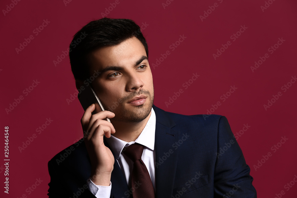 Portrait of handsome young businessman with mobile phone on color background