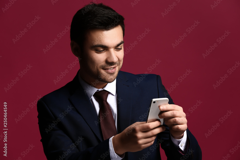 Portrait of handsome young businessman with mobile phone on color background